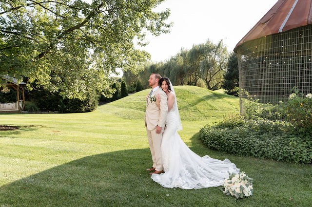 Bride and groom in a green garden beside a barn