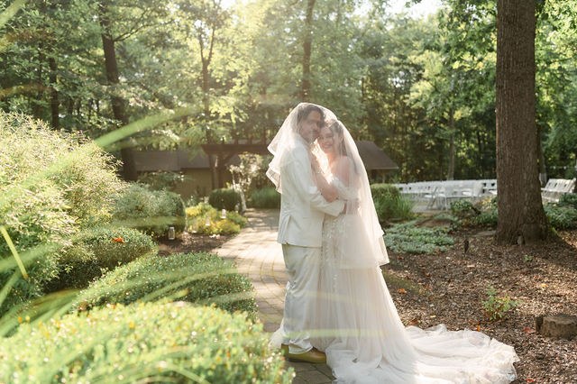 Bride and groom beneath a veil in a sunlit garden
