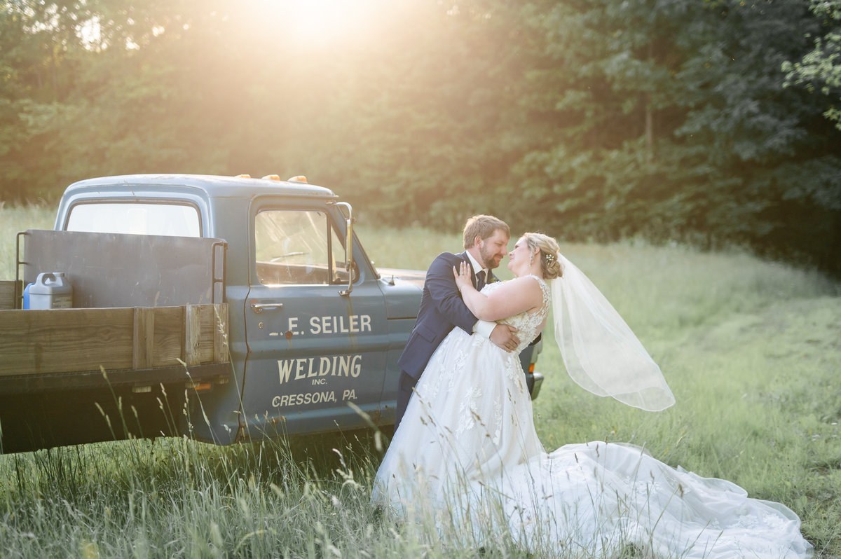 Newlyweds beside a vintage truck in evening light